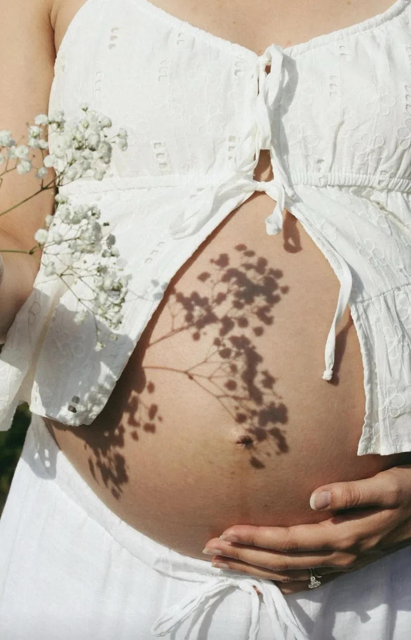 Schwangerer Bauch mit Schleierkraut im Sonnenlicht
